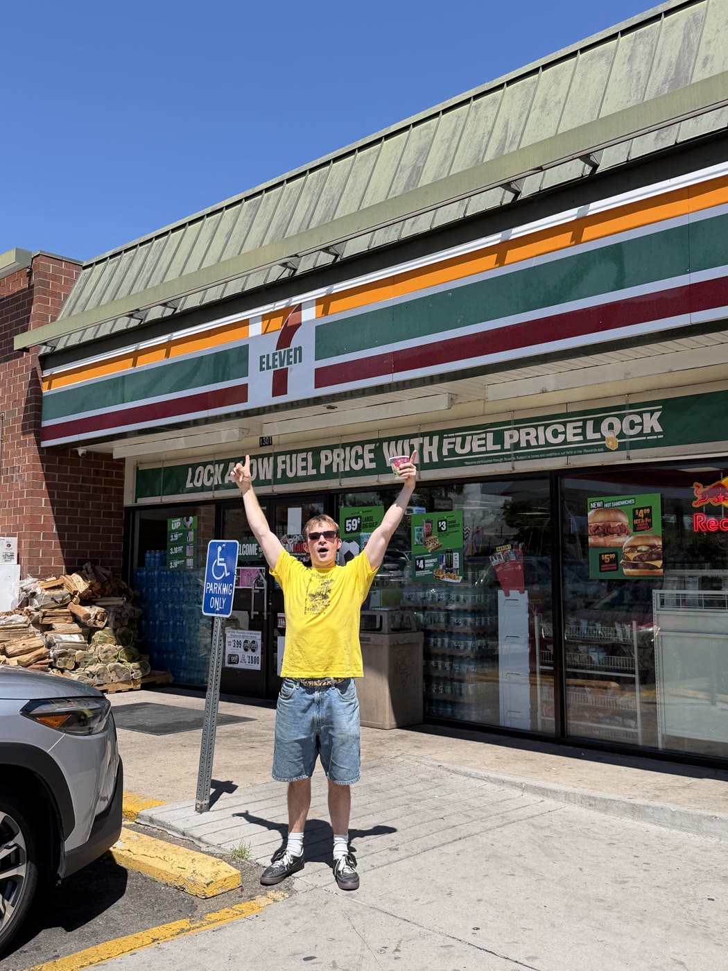 Marc outside a 7-Eleven, holding a drink with both arms raised